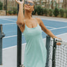 Full body front view of model wearing the Traveler Mini Dress in Sage that has sage green fabric, shorts lining with side pockets, bra padding, a scoop  neck, and straps that cross in the back