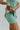Side shorts view of model wearing the Traveler Mini Dress in Sage that has sage green fabric, shorts lining with side pockets, bra padding, a scoop  neck, and straps that cross in the back