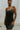 Front view of model wearing the Traveler Mini Dress in Black that has lightweight fabric, a mini-length hem, shorts lining with side pockets, bra padding, a scoop neck, and straps that cross in the back.