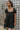Front view of model wearing the Change Your Mind Dress that has black textured fabric, mini length, a ruffle hem, a square neckline, short puff sleeves with elastic bands, a back tie strap, and black lining.