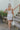 Full body back view of model wearing the Now and Forever Dress that has white fabric, a mini-length hem, a white lining, a round neckline, ruffle/elastic straps and a monochromatic side zipper.