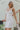 Front view of model wearing the Now and Forever Dress that has white fabric, a mini-length hem, a white lining, a round neckline, ruffle/elastic straps and a monochromatic side zipper.