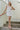 Full body front view of model wearing the Now and Forever Dress that has white fabric, a mini-length hem, a white lining, a round neckline, ruffle/elastic straps and a monochromatic side zipper.