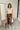 Full body front view of model wearing the Trouble Maker Pleather Midi Skirt that has dark brown faux leather, midi length, a slit, pockets, a front zipper, and belt loops