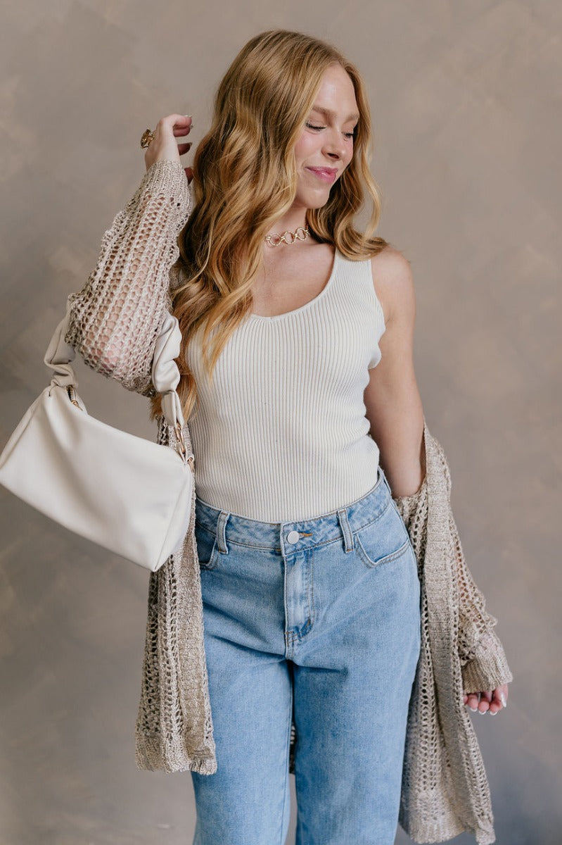 Front view of model wearing the Remington Beige Crochet Knit Cardigan which features beige open knit fabric, a front opening with no closure, a thick hem, two front pockets, and long sleeves.