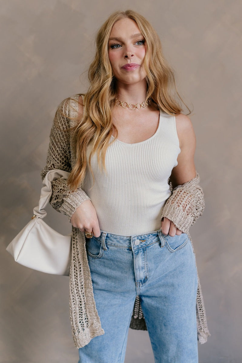 Front view of model wearing the Remington Beige Crochet Knit Cardigan which features beige open knit fabric, a front opening with no closure, a thick hem, two front pockets, and long sleeves.