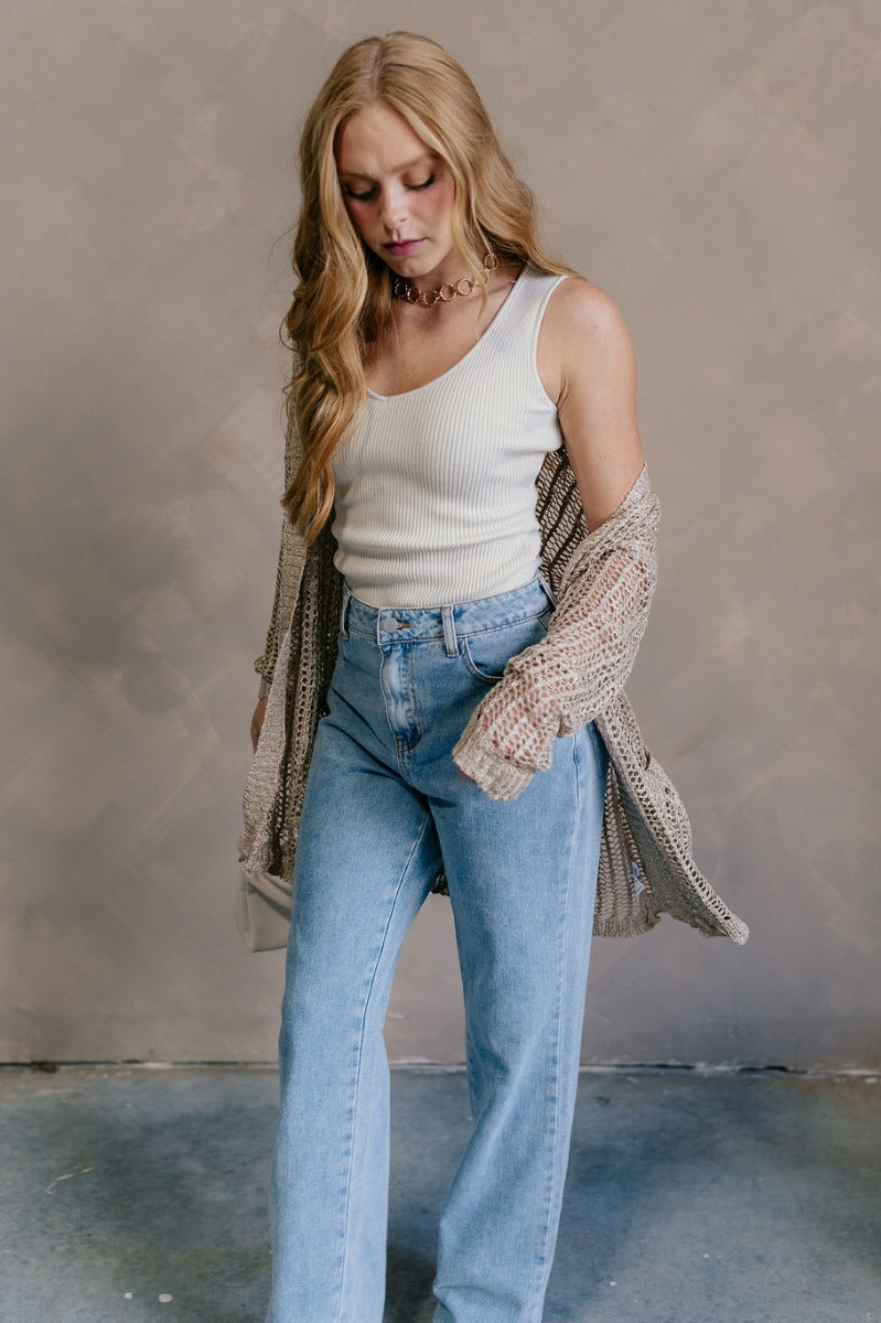 Full body view of model wearing the Remington Beige Crochet Knit Cardigan which features beige open knit fabric, a front opening with no closure, a thick hem, two front pockets, and long sleeves.