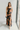 Full body view of model wearing the Athena Black Multi Floral Slit Maxi Dress which features black satin fabric with a red, orange, and green rose floral pattern, maxi length, a slit on the side, a cowl neckline, adjustable spaghetti straps, and an open b