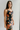 Side view of model wearing the Athena Black Multi Floral Slit Maxi Dress which features black satin fabric with a red, orange, and green rose floral pattern, maxi length, a slit on the side, a cowl neckline, adjustable spaghetti straps, and an open back w