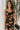 Front view of model wearing the Athena Black Multi Floral Slit Maxi Dress which features black satin fabric with a red, orange, and green rose floral pattern, maxi length, a slit on the side, a cowl neckline, adjustable spaghetti straps, and an open back 