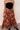 Front view of model wearing the Catalina Rust Multi Floral Maxi Skirt which features rust sheer fabric with mustard, blue, green, pink and white floral print, metallic thread details, rust lining, midi length, an elastic waistband, belt loops, and a tie c