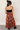 Full body back view of model wearing the Catalina Rust Multi Floral Maxi Skirt which features rust sheer fabric with mustard, blue, green, pink and white floral print, metallic thread details, rust lining, midi length, an elastic waistband, belt loops, an