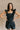 Front view of model wearing the Avril Black Denim Ruffle Sleeveless Romper which features black washed denim fabric, pockets on each side, a front zip up, an elastic waistband, a square neckline, and ruffle straps.