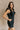 Front side view of model wearing the Avril Black Denim Ruffle Sleeveless Romper which features black washed denim fabric, pockets on each side, a front zip up, an elastic waistband, a square neckline, and ruffle straps.
