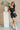 Full body view of model wearing the Avril Black Denim Ruffle Sleeveless Romper which features black washed denim fabric, pockets on each side, a front zip up, an elastic waistband, a square neckline, and ruffle straps.