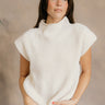 Front view of model wearing the Blakely Cream High Neck Sleeveless Sweater which features cream cable knit fabric, a thick hem, a high neckline and a sleeveless design.