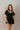 front view of model wearing the Eliana Black Tiered Short Sleeve Romper that has black lightweight fabric, a ruffle-tiered skirt, black shorts lining, an elastic waistband, a sweetheart neckline and short puff sleeves.