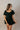 front view of model wearing the Eliana Black Tiered Short Sleeve Romper that has black lightweight fabric, a ruffle-tiered skirt, black shorts lining, an elastic waistband, a sweetheart neckline and short puff sleeves.
