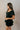 Side view of model wearing the Eliana Black Tiered Short Sleeve Romper that has black lightweight fabric, a ruffle-tiered skirt, black shorts lining, an elastic waistband, a sweetheart neckline and short puff sleeves.