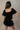 Back view of model wearing the Eliana Black Tiered Short Sleeve Romper that has black lightweight fabric, a ruffle-tiered skirt, black shorts lining, an elastic waistband, a sweetheart neckline and short puff sleeves.