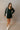Full body front view of model wearing the Adalynn Black Textured Knit Mini Dress that has black textured fabric, pockets, a v-neckline, and long wide sleeves with layered cuffs.