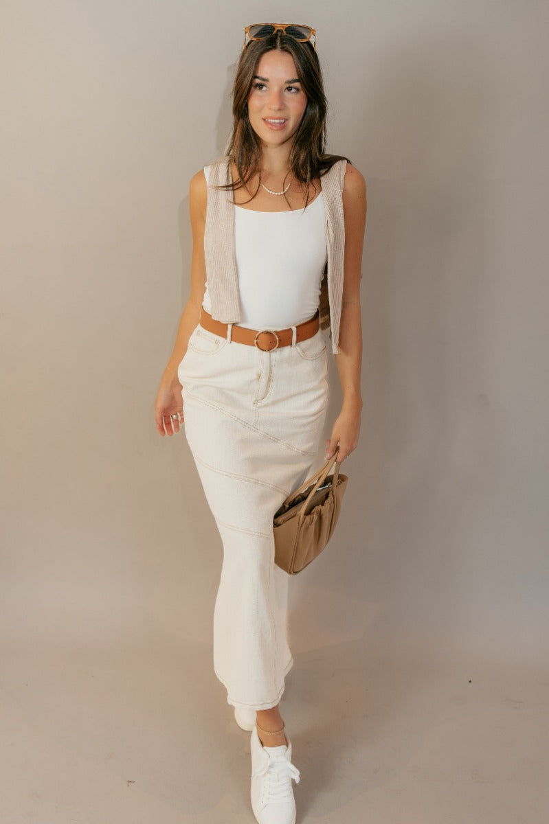 The Esther Cream Denim Midi Skirt features cream denim fabric with brown stitched geometric pattern, midi length, a front zipper with a button closure, belt loops, two front pockets, and two back pockets.