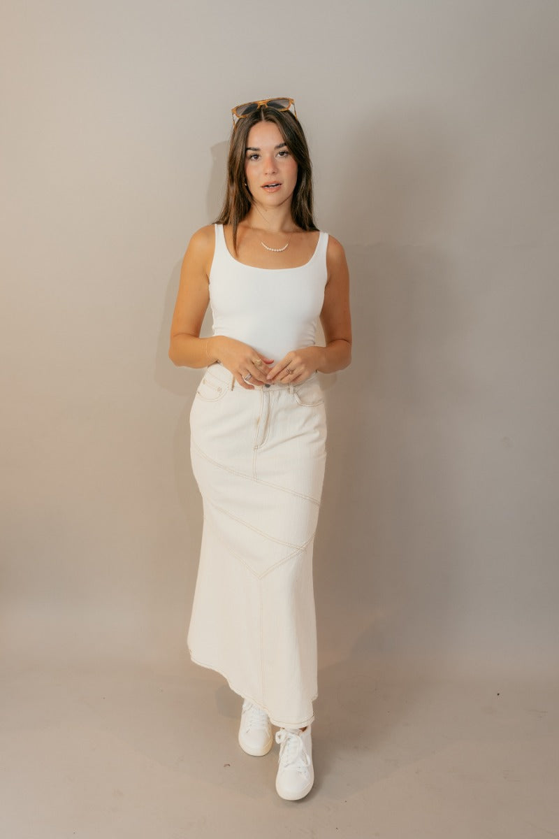 Full body front view of model wearing the Esther Cream Denim Midi Skirt that has cream denim fabric with brown stitched geometric pattern, belt loops, and pockets.