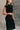 Side view of model wearing the Lenora Black Knit High-Neck Midi Dress that has black knit fabric, midi length, a high neckline and a sleeveless design.