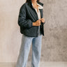 Full body front view of model wearing the Lakelyn Charcoal Grey Quilted Jacket that has charcoal grey fabric with a quilted diamond pattern, pockets, tortoise buttons, a high neckline, and long sleeves.