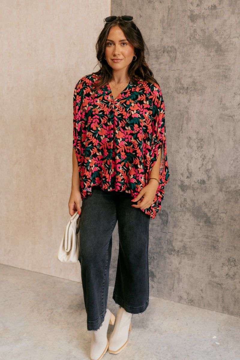Full body front view of model wearing the Rowyn Black & Multi Floral Print Oversized Top that has black fabric with a floral print, a round neckline with v cut-out, and short dolman sleeves.