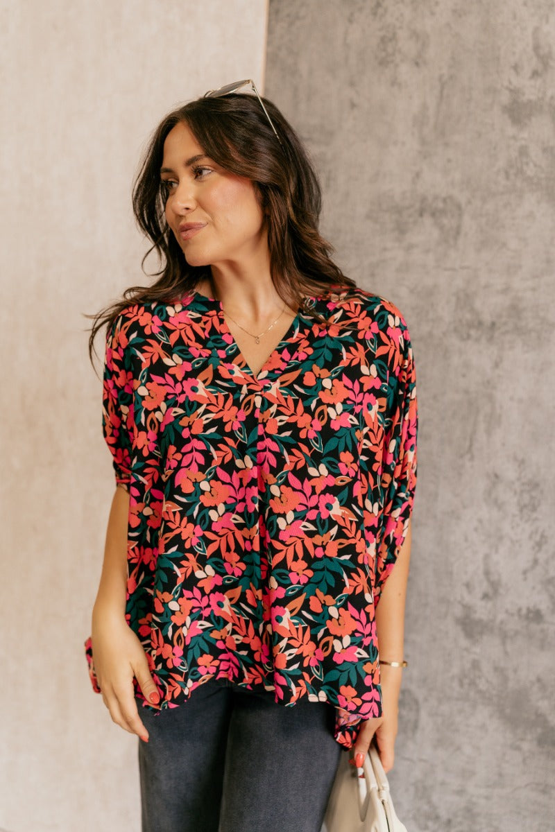 front view of model wearing the Rowyn Black & Multi Floral Print Oversized Top that has black fabric with a floral print, a round neckline with v cut-out, and short dolman sleeves.