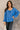 Front view of model wearing the Audrey Blue Satin Adjustable Neckline Long Sleeve Top which features blue satin fabric, a round neckline with drawstring tie, and long balloon sleeves with elastic wrists.