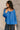 Front view of model wearing the Audrey Blue Satin Adjustable Neckline Long Sleeve Top which features blue satin fabric, a round neckline with drawstring tie, and long balloon sleeves with elastic wrists.