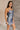 Side view of model wearing the Amber Blue Cowl Neckline Sleeveless Mini Dress which features blue shimmer fabric, mini length, blue lining, a cowl neckline, adjustable straps, and a monochromatic back zipper with a hook closure.