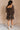 Full body back view of model wearing the Aurora Black Multi Floral Long Sleeve Mini Dress which features black sheer fabric with red, orange, and grey floral print, black lining, mini length, a square neckline, long balloon sleeves with elastic wrists, an