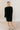 Full body back view of model wearing the Sara Black Long Sleeve T-shirt Dress that has black cotton fabric, mini length, slits on each side, a round neckline, dropped shoulders, and long sleeves.