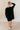 Full body back view of model wearing the Sara Black Long Sleeve T-shirt Dress that has black cotton fabric, mini length, slits on each side, a round neckline, dropped shoulders, and long sleeves.