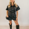 Full body front view of model wearing the Ruth Black Denim Short Sleeve Romper that has washed black denim fabric, pockets, brown stitching, a front zipper, a collared neckline, belt loops, and short sleeves.