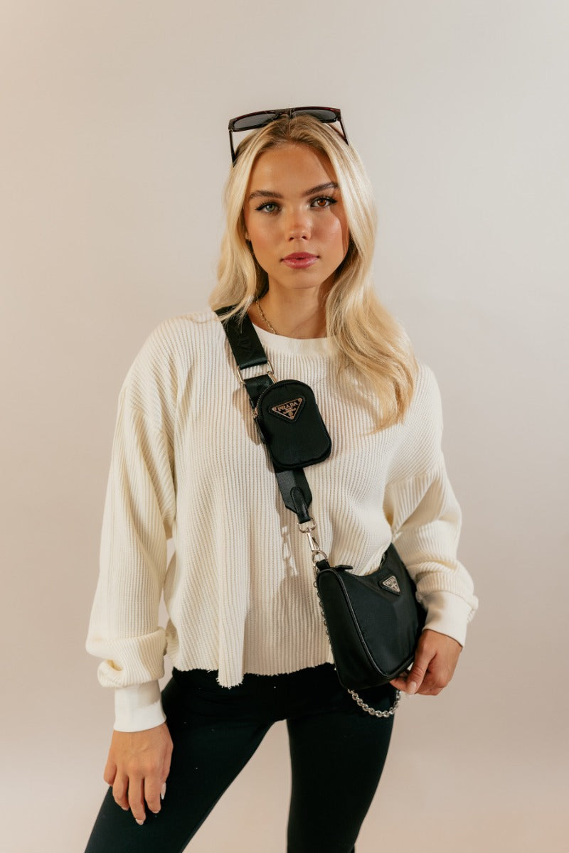 front view of model wearing the Ada Cream Waffle-Knit Long Sleeve Top that features cream waffle knit fabric, a raw hem, a round neckline, dropped shoulders, and long sleeves with cuffs.