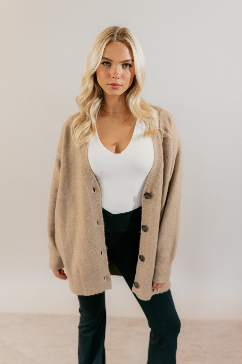 front view of model wearing the Oaklynn Mocha Oversized Cardigan that has mocha brown knit fabric, ribbed hem, a button-up front with dark tortoise buttons, a v-neckline, and long sleeves with cuffs.