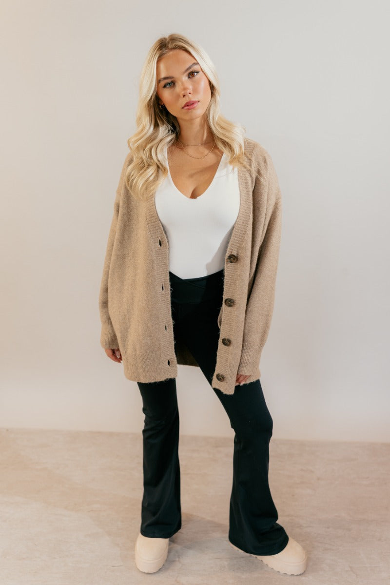 Full body unbuttoned front view of model wearing the Oaklynn Mocha Oversized Cardigan that has mocha brown knit fabric, ribbed hem, a button-up front with dark tortoise buttons, a v-neckline, and long sleeves with cuffs.