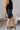 Side view of model wearing the Miley Black Rhinestone Faux Leather Mini Skirt which features black faux leather fabric, black lining, mini length, rhinestone embellishments, and a monochromatic side zipper with a hook closure.