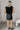 Full body back view of model wearing the Miley Black Rhinestone Faux Leather Mini Skirt which features black faux leather fabric, black lining, mini length, rhinestone embellishments, and a monochromatic side zipper with a hook closure.