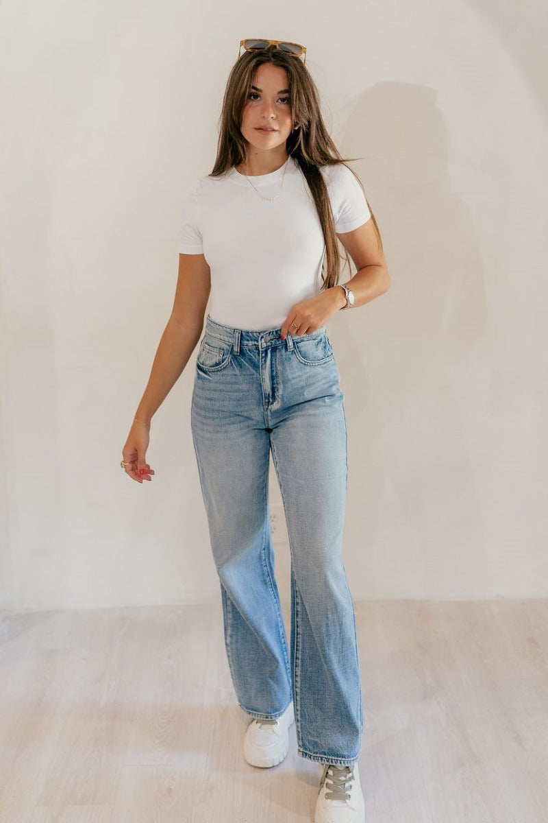 Full body front view of model wearing the The Rooted Denim: Camila Wide Leg Jeans that have light medium denim fabric, a front zipper with a button closure, belt loops, pockets and wide legs.