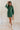 Full body front view of model wearing the Gianna Dark Green Button Front Dress that has dark green corduroy fabric, white stitch detailing, front button closures, a collared neck, chest pockets, and long sleeves.