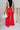 Full body back view of model wearing the Scarlett Red Wide Leg Pants which features red lightweight fabric, two front pockets, a front zipper with a hook closure, belt loops and wide legs.