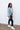 Full body side view of model wearing the Time Is Now Cardigan that has teal, white, and light green knit fabric with a stitched pattern, a button-up front, long sleeves, and a cropped waist. Worn unbuttoned over brami.