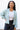 Front view of model wearing the Time Is Now Cardigan that has teal, white, and light green knit fabric with a stitched pattern, a button-up front, long sleeves, and a cropped waist. Worn unbuttoned over brami.