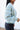Side view of model wearing the Time Is Now Cardigan that has teal, white, and light green knit fabric with a stitched pattern, a button-up front, long sleeves, and a cropped waist.