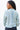 Back view of model wearing the Time Is Now Cardigan that has teal, white, and light green knit fabric with a stitched pattern, a button-up front, long sleeves, and a cropped waist.